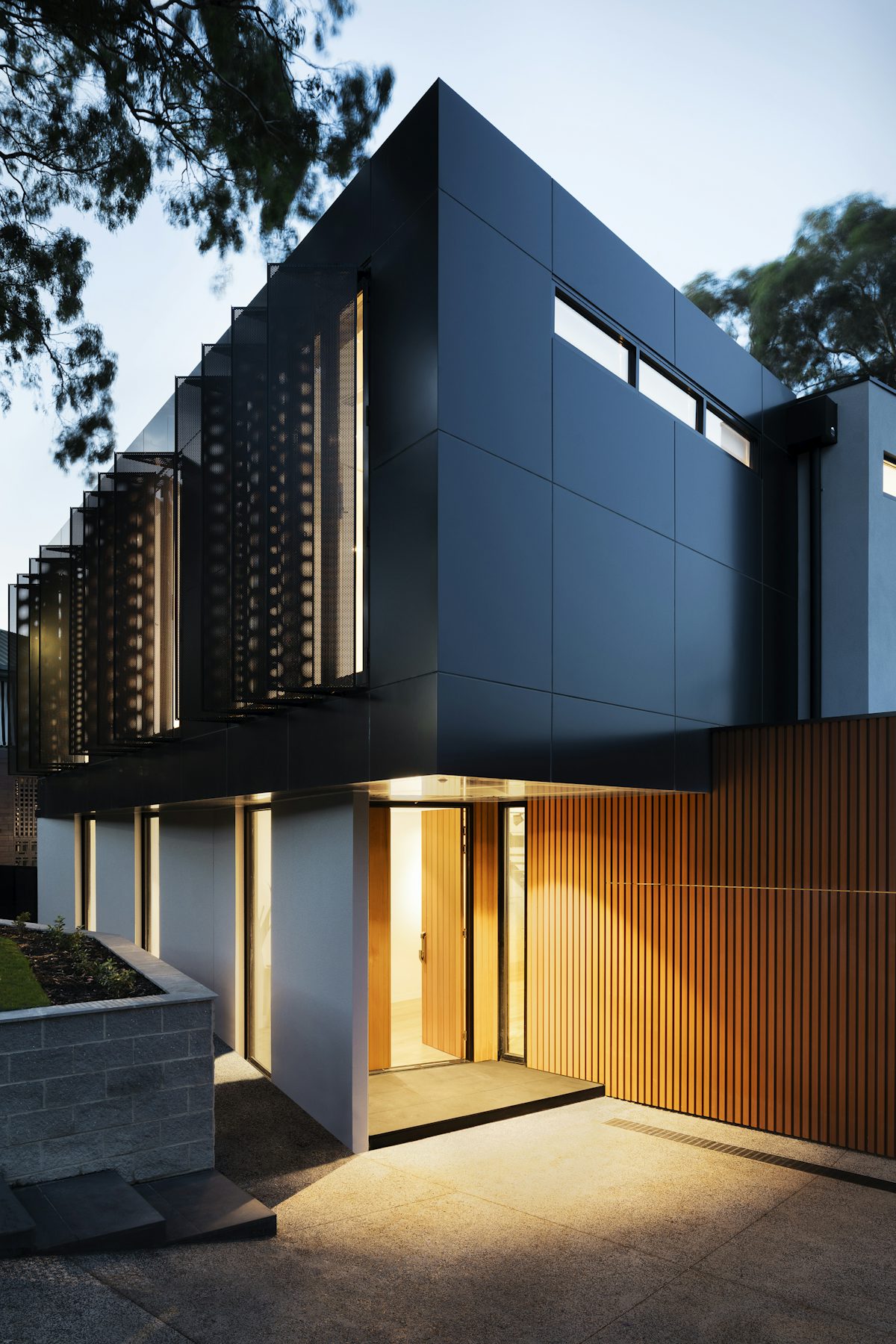 Villa d'architecte contemporaine à la tombée du jour, façade en bois et béton, entrée éclairée